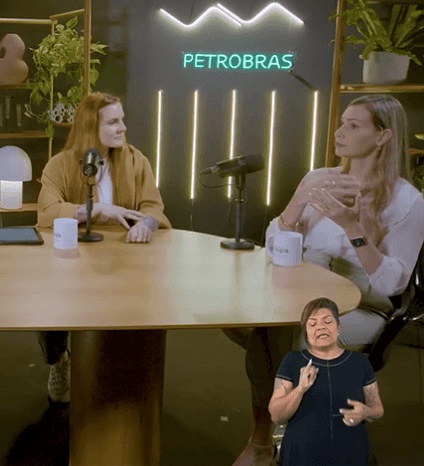 Duas mulheres sentadas em um estúdio, com microfones em sua frente.