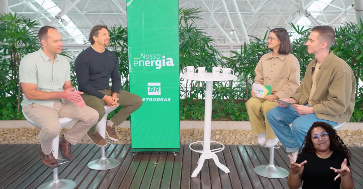 Quatro pessoas conversam em um estúdio com painel “Nossa energia Petrobras” ao centro, enquanto intérprete de Libras aparece no canto inferior direito.