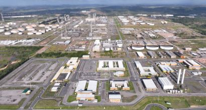 Vista aérea da Refinaria Abreu e Lima (RNEST), em Pernambuco, com tanques, torres de processamento e estruturas industriais cercados por vegetação.