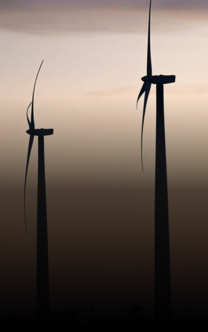Fileira de turbinas eólicas em silhueta ao pôr do sol com texto "A importância das energias renováveis".