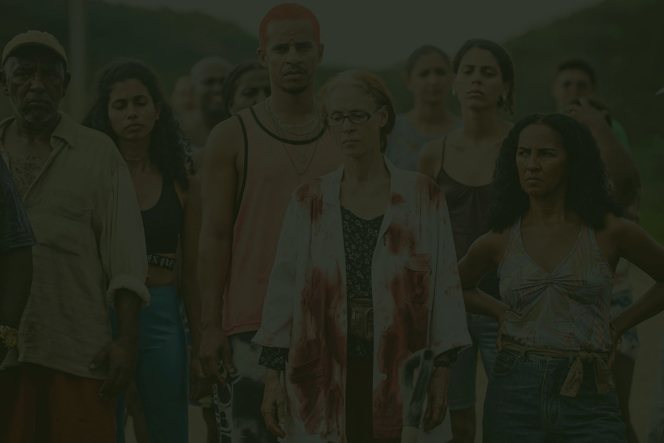 Grupo de pessoas com expressões sérias; mulher ao centro veste jaleco manchado.