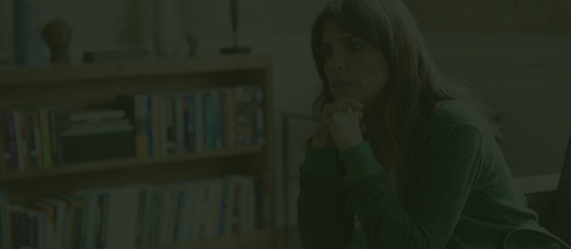 Mulher pensativa com as mãos no rosto em frente a uma estante.