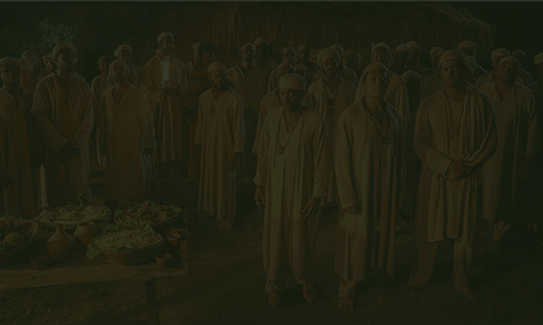 Grupo de homens negros com vestes claras e gorros em cena noturna.