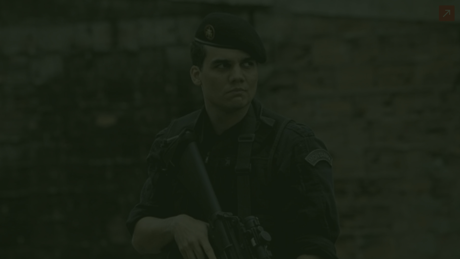 Capitão Nascimento fardado e segurando um fuzil, com olhar atento para o lado, em cena de