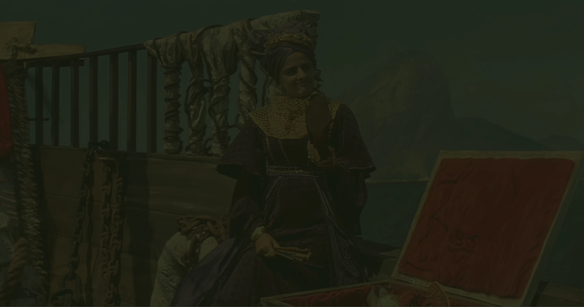 Marieta Severo, caracterizada como Carlota Joaquina com vestido e turbante roxos, sentada em um navio com o Pão de Açúcar ao fundo. Ela segura um sapato e há um baú aberto à sua frente.