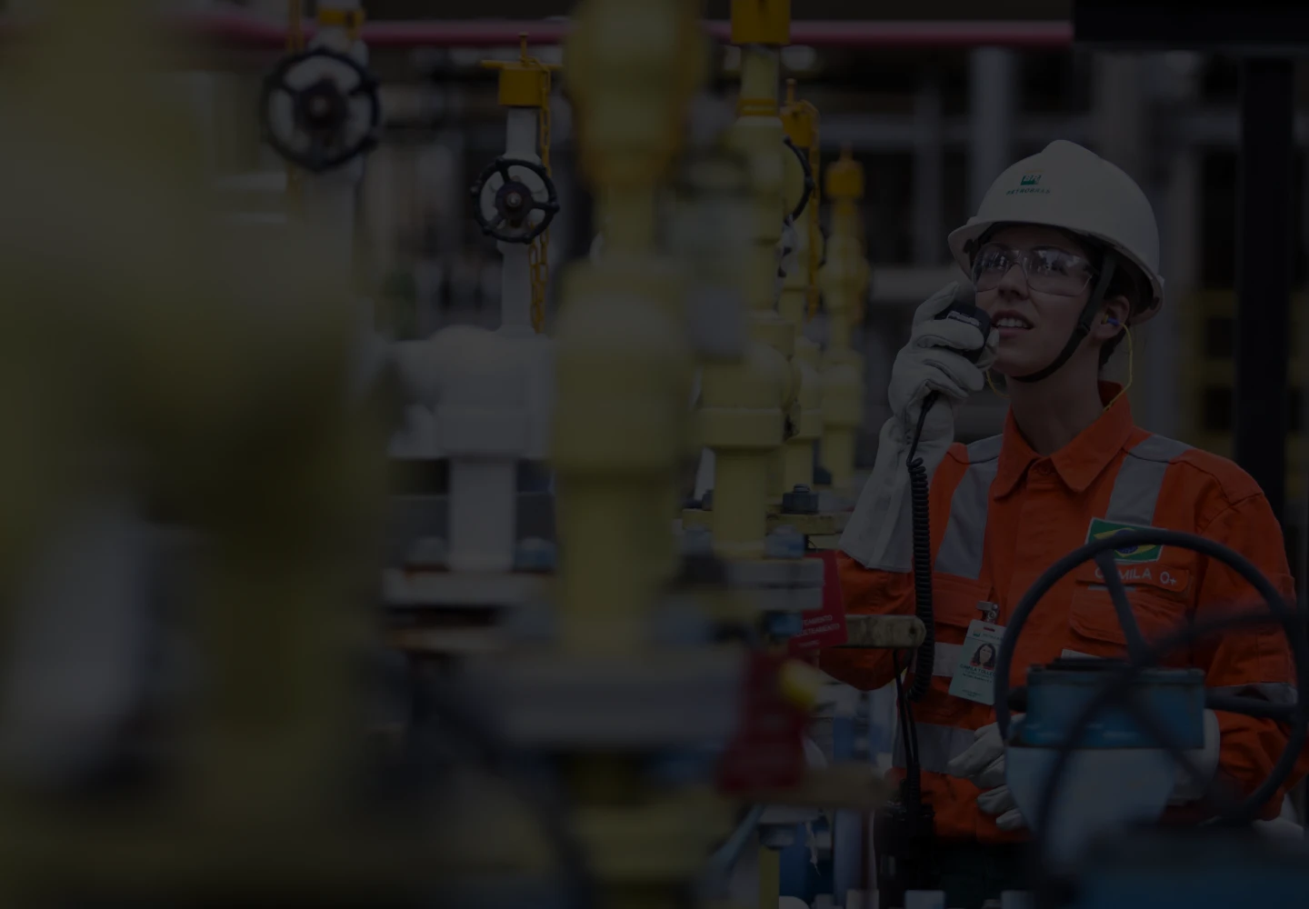 Daytime photo of a Petrobras employee wearing full personal protective equipment and talking into a walkie-talkie.