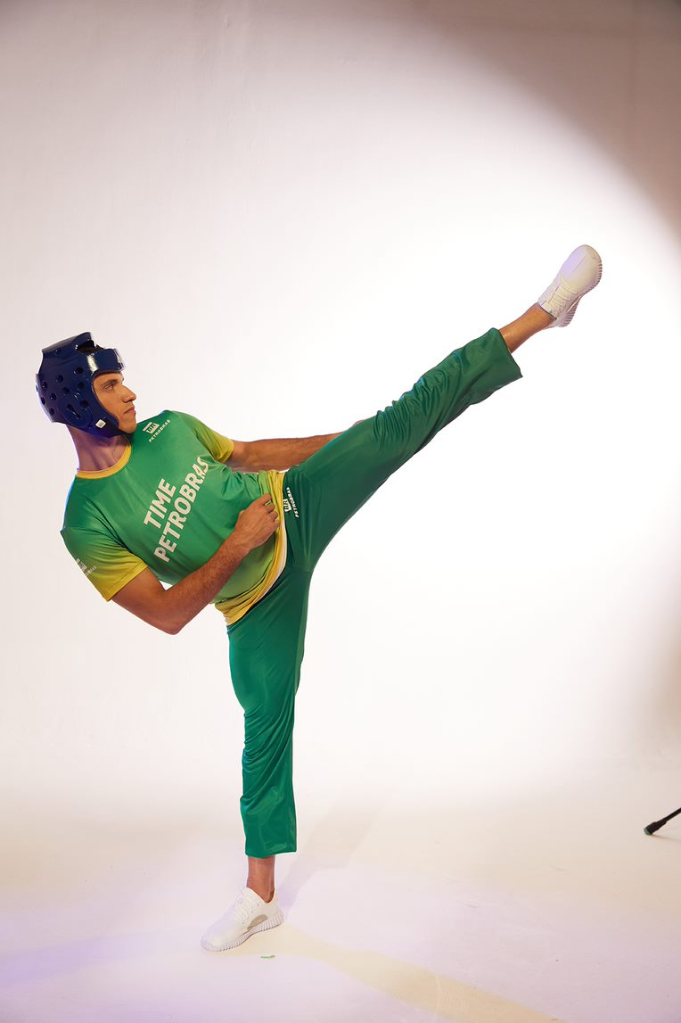 Homem com camiseta do Time Petrobras praticando chute de taekwondo.