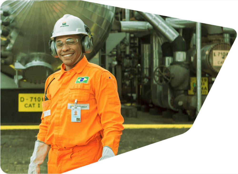 Employee with a career at Petrobras smiles at the camera, wearing uniform and full protective equipment.