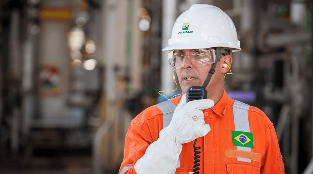 Funcionário da Petrobras usando equipamento de proteção individual completo e falando a um walkie talkie.