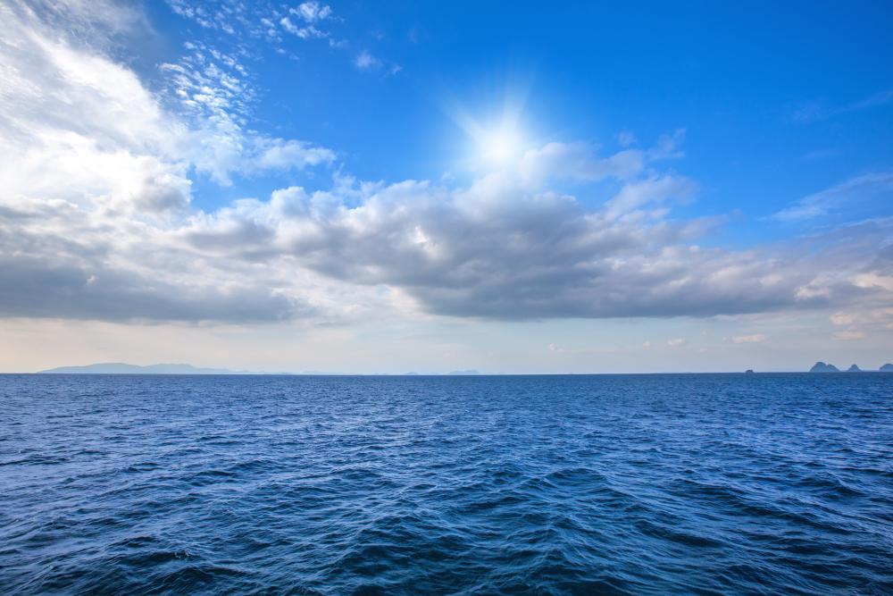 Foto diurna do horizonte entre o mar e o céu azul, com nuvens.