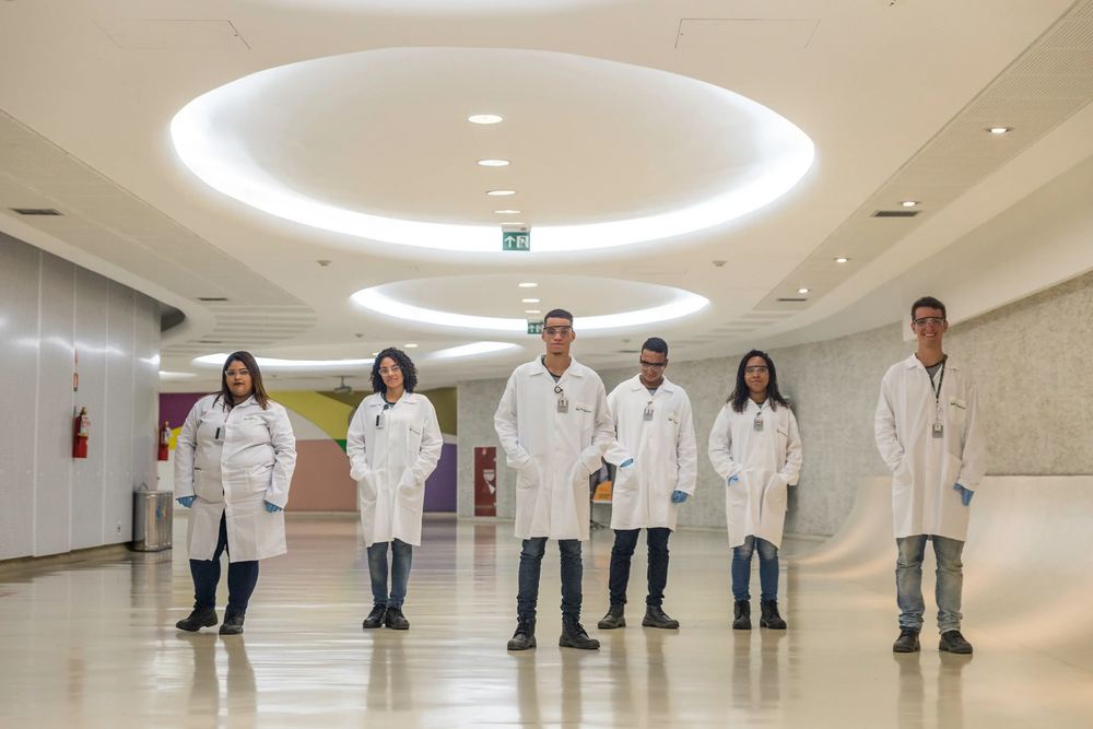 Seis jovens aprendizes da Petrobras em pé em um corredor iluminado do Cenpes.