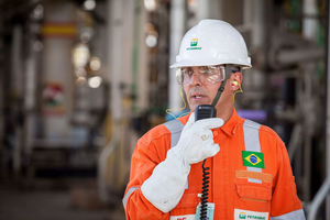Funcionário da Petrobras usando equipamento de proteção individual completo e falando a um walkie talkie.