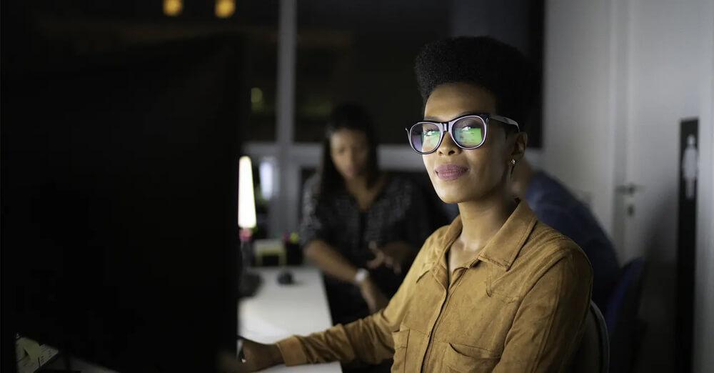 mulher negra sentada na frente de um monitor de computador