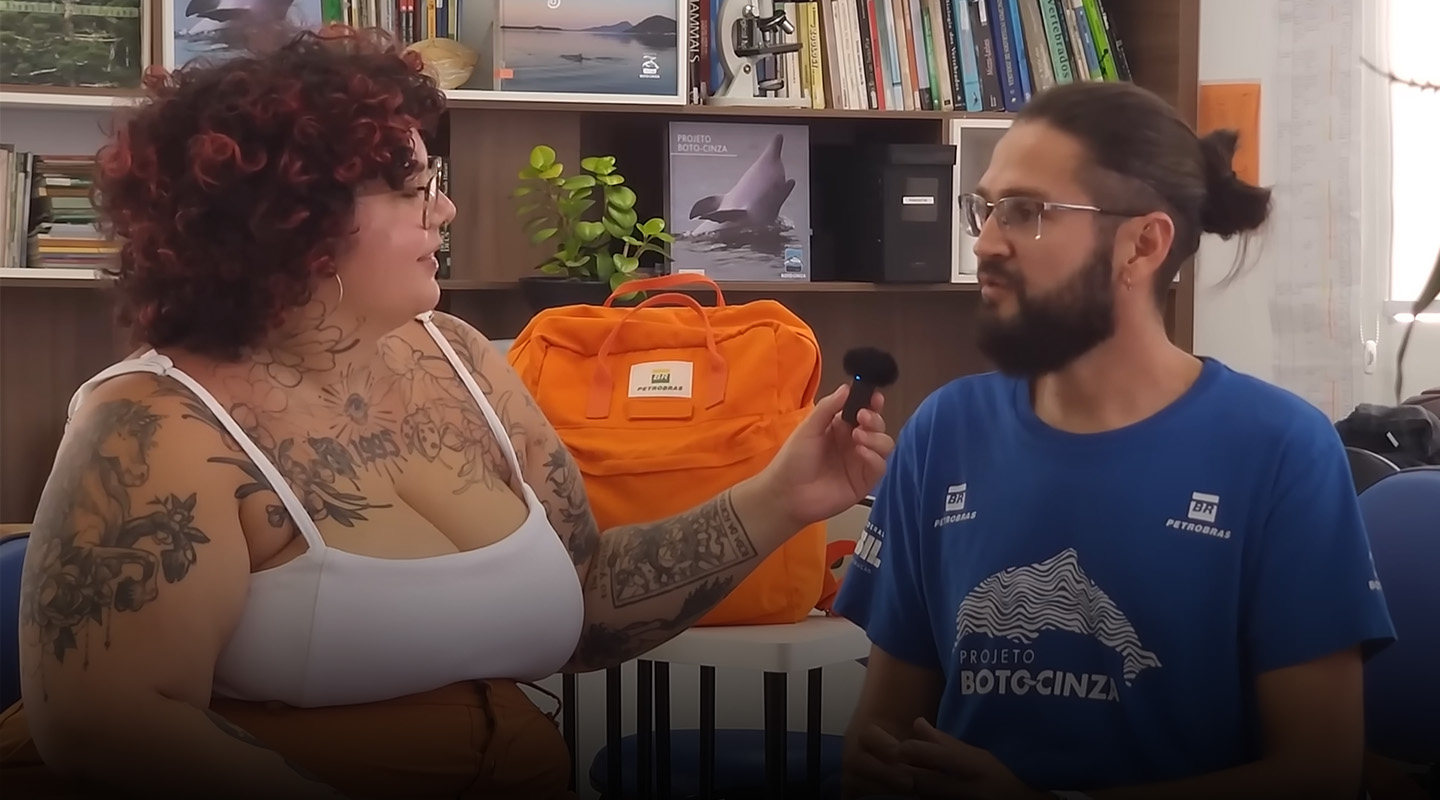 Mulher entrevistando um homem, com um pequeno microfone na mão esquerda.