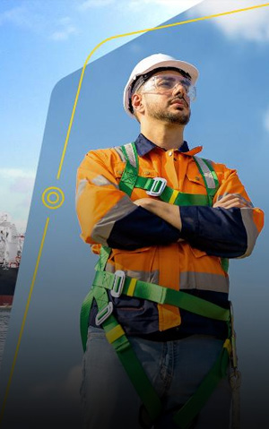 A imagem apresenta um navio, identificado como "Jorge Amado", ancorado em um corpo de água. O navio é de grande porte e tem um casco preto, com detalhes em vermelho e algumas bandeiras visíveis no mastro. Ao fundo, há um céu azul com algumas nuvens. No primeiro plano, um trabalhador está posicionado à direita, usando um capacete branco, óculos de segurança, e um uniforme laranja.