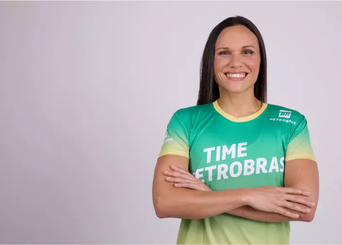 Mulher com os braços cruzados vestindo camiseta verde e amarela do Time Petrobras.